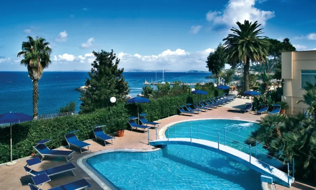 Piscine esterne con lettini e ombrelloni blu affacciate sul mare e sul porto