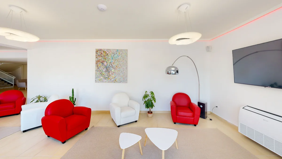Hall con poltrone rosse e bianche, TV a parete e quadro colorato