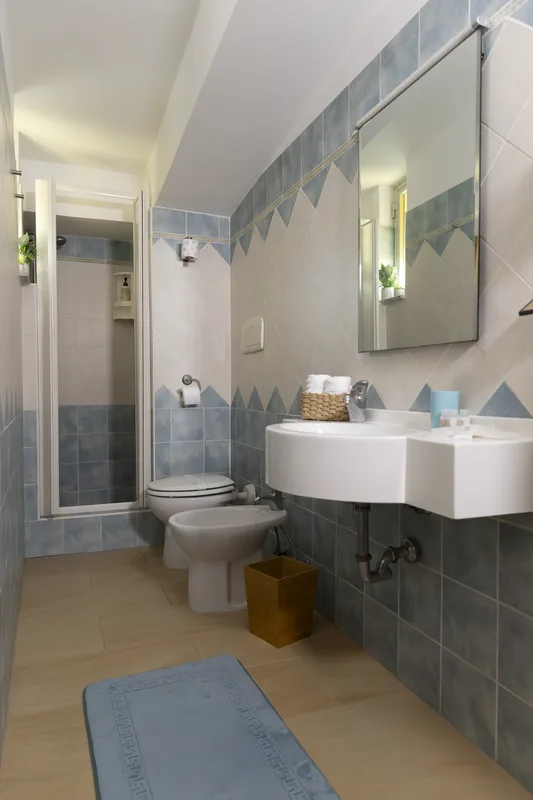 Bagno con piastrelle azzurre, doccia, lavabo e bidet