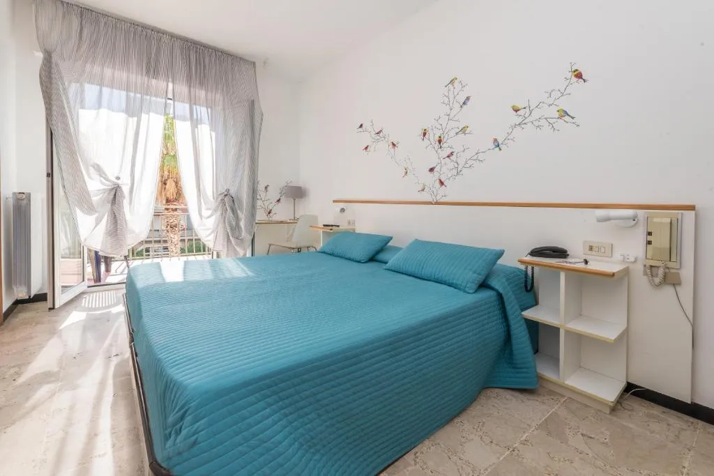 Camera con letto matrimoniale e copriletto turchese, balcone luminoso e decorazioni di uccelli sulla parete