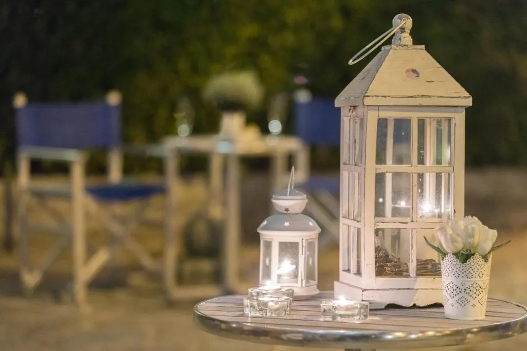 Dettaglio di lanterne bianche e candele su tavolino in giardino con sedie blu in serata romantica