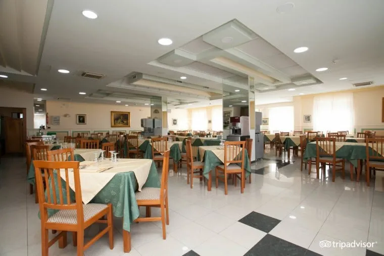 Sala ristorante con tavoli apparecchiati e tovaglie verdi e bianche