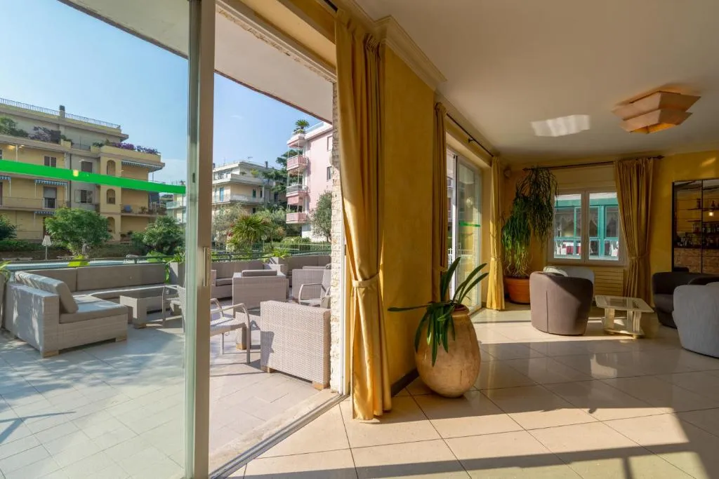 Hall luminosa con divani, ampie vetrate e terrazza esterna con poltrone