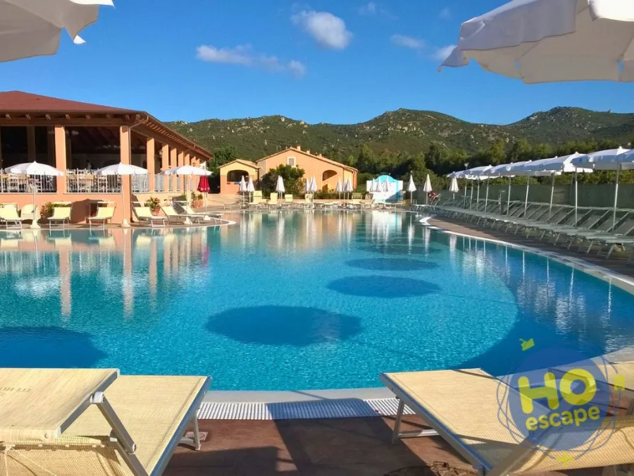Ampia piscina del resort con lettini, ombrelloni bianchi e colline verdi sullo sfondo