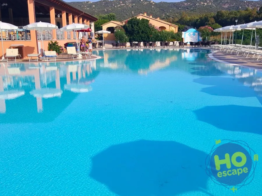 Grande piscina del resort con area bar, ombrelloni e colline alle spalle