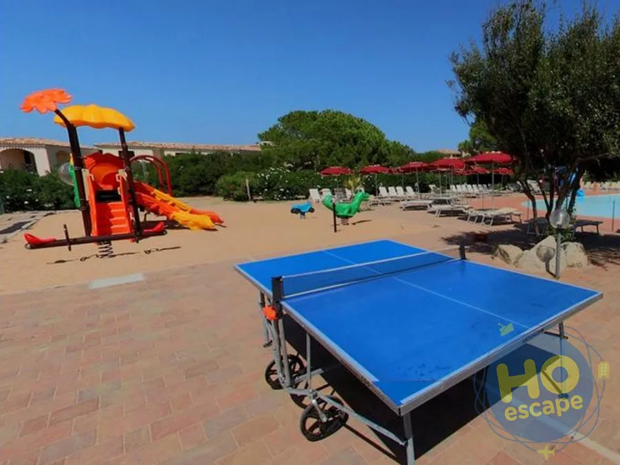 Area esterna con tavolo da ping pong, parco giochi colorato e piscina sullo sfondo