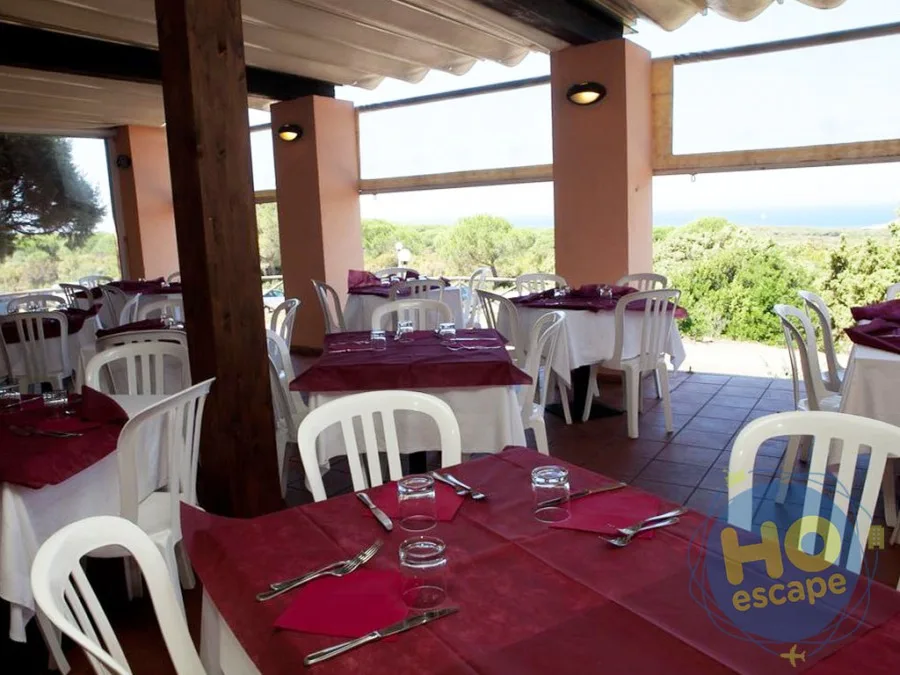 Sala ristorante con terrazza coperta, tavoli con tovaglie bordeaux e vista sulla macchia mediterranea e mare