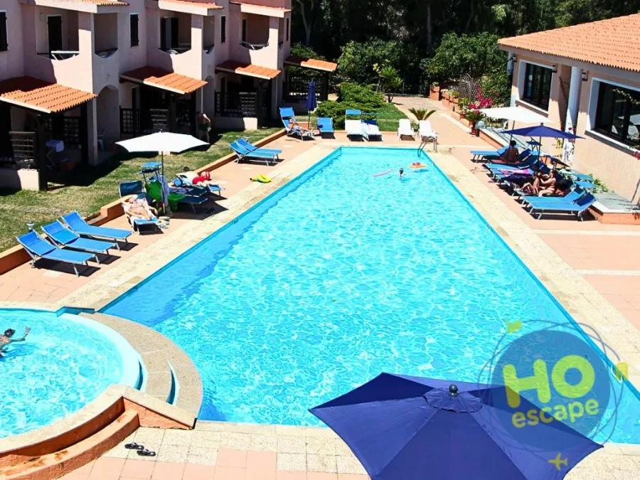 Piscina con vasca idromassaggio, lettini blu e ombrelloni tra le villette