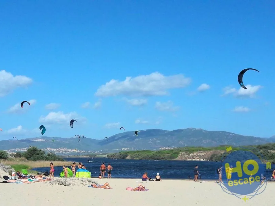 Spiaggia con kitesurf e aquiloni colorati sopra la laguna con colline sullo sfondo