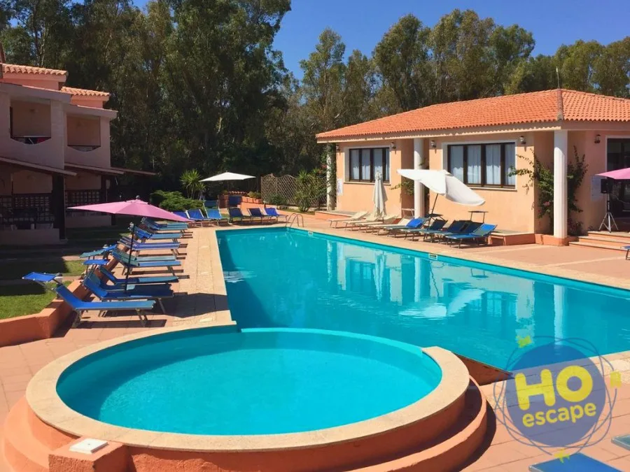 Piscina esterna con piscina per bambini rotonda, lettini blu e ombrelloni colorati circondata da edifici color pesca