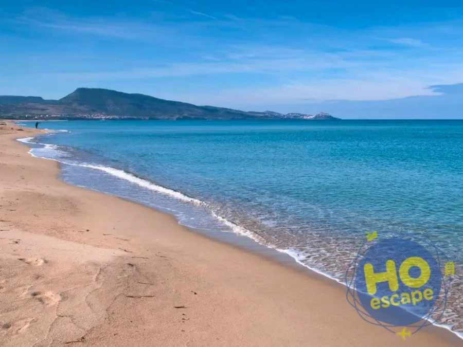Spiaggia di sabbia dorata con mare azzurro cristallino e promontorio sullo sfondo