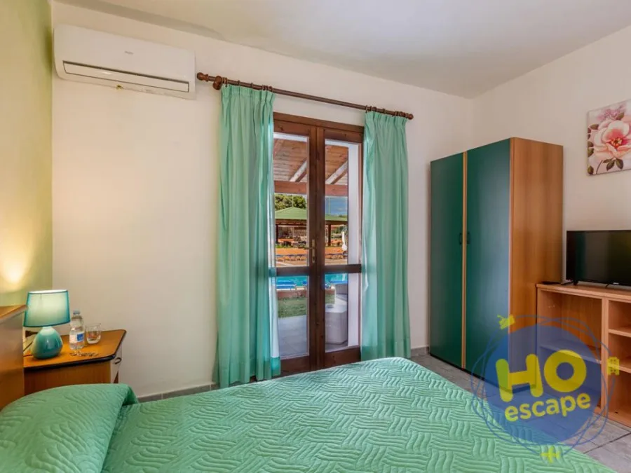 Camera con letto, armadio verde e TV con porta finestra sul giardino