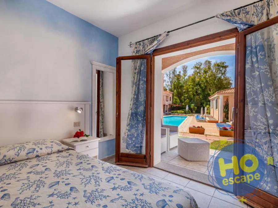 Camera da letto con pareti azzurre e copriletto a tema marino, con porta finestra che si affaccia sulla piscina e il giardino
