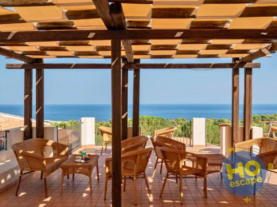 Terrazza con pergolato in legno, poltrone in vimini e vista panoramica sul mare