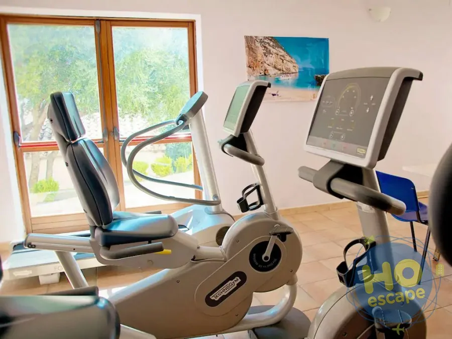 Sala fitness con cyclette e attrezzi Technogym vicino a grandi finestre con vista sul verde