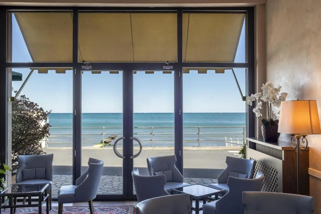 Sala salotto con poltrone azzurre e grande vetrata affacciata sul lungomare e il mare