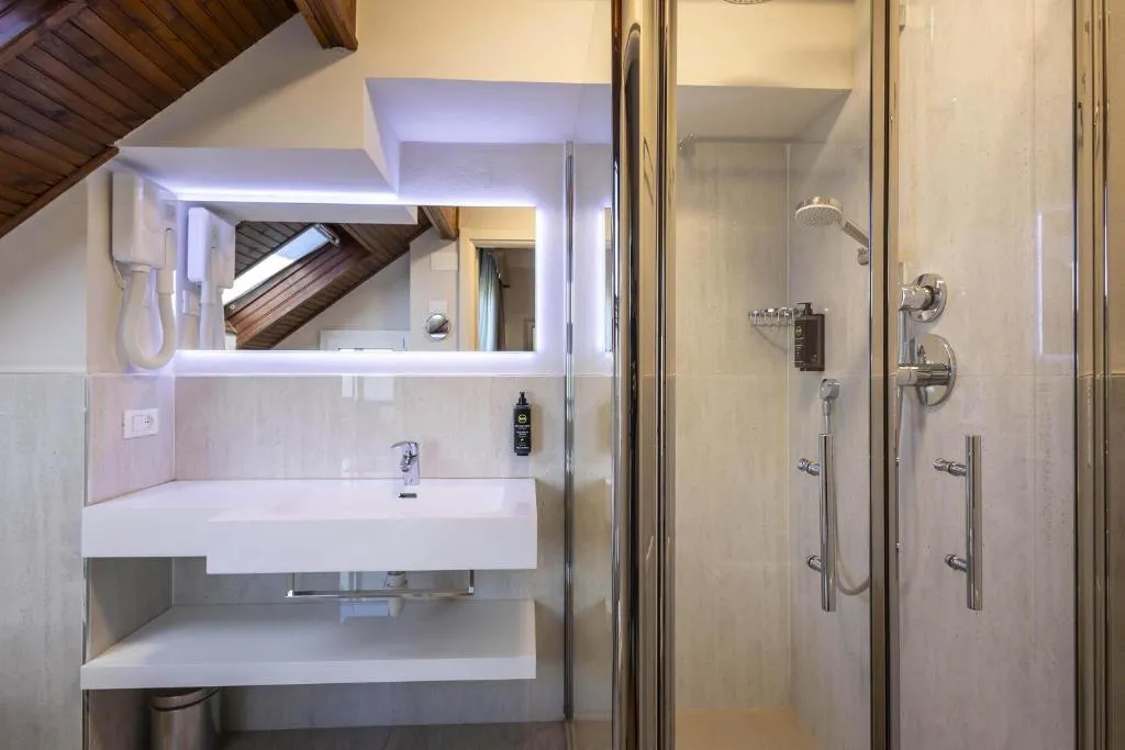 Bagno mansardato con doccia in vetro, lavabo bianco sospeso e illuminazione a led
