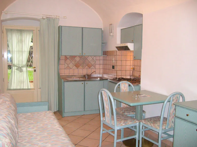 Cucina con angolo cottura verde acqua, tavolo da pranzo e porta finestra