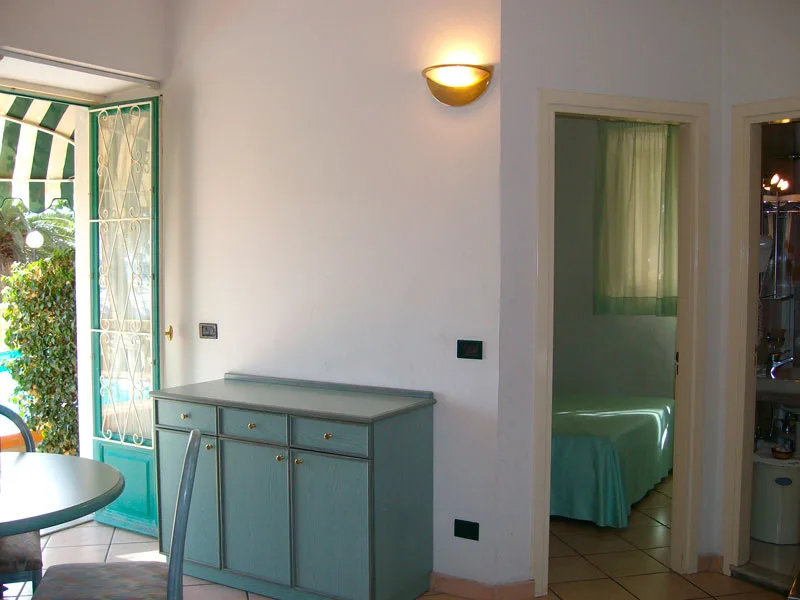 Soggiorno con credenza verde, accesso esterno e camera da letto adiacente