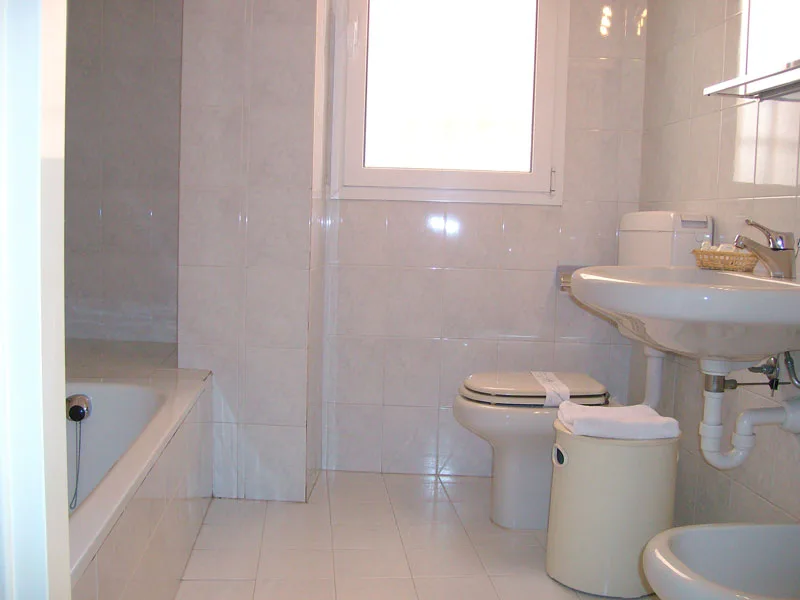 Bagno piastrellato con vasca, lavabo, wc e finestra