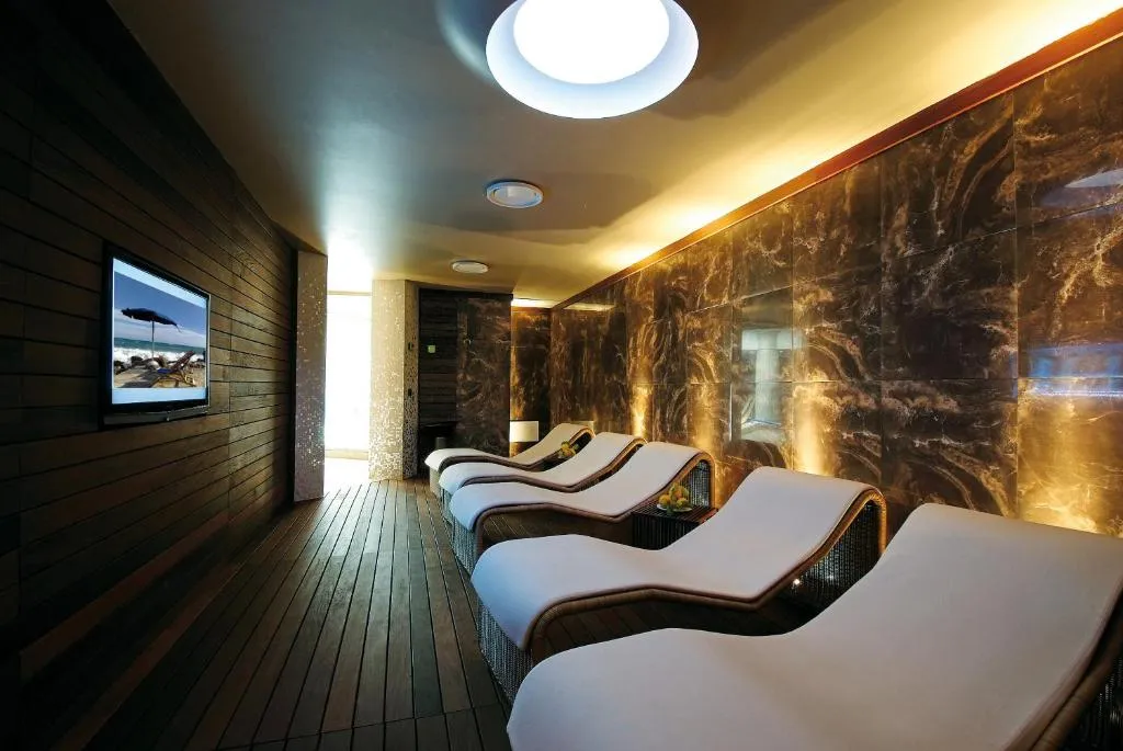 Zona relax della spa con lettini ergonomici, pareti in marmo e schermo TV