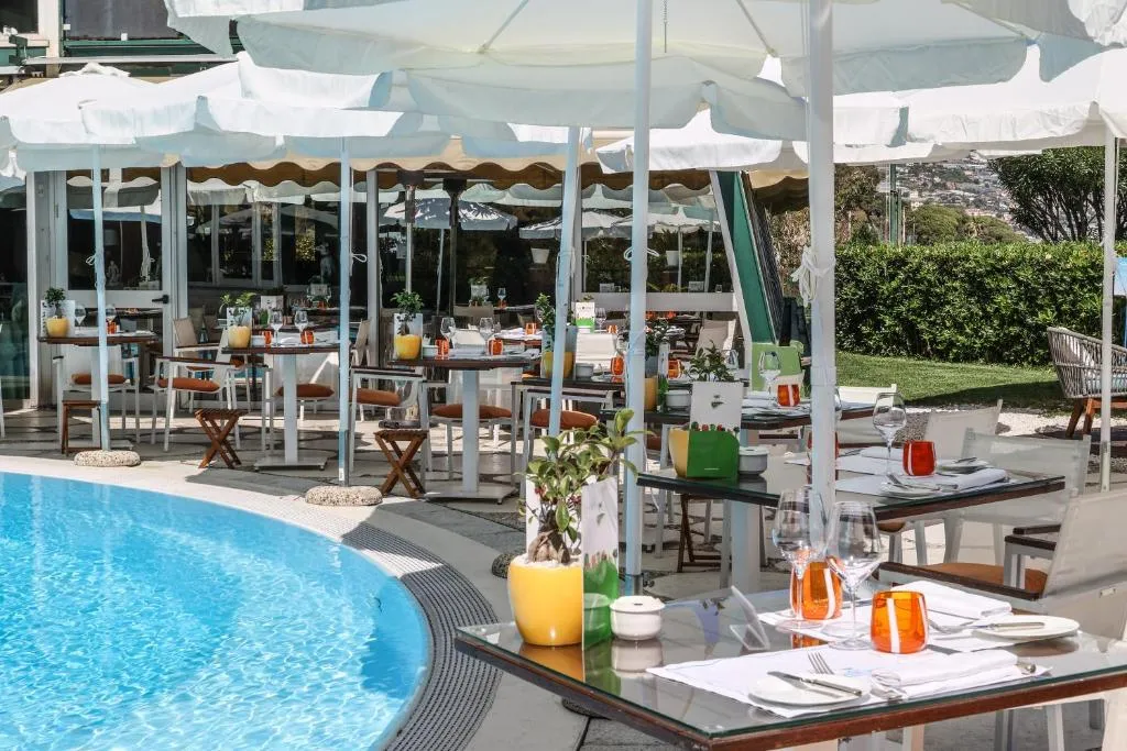 Ristorante all'aperto a bordo piscina con tavoli apparecchiati e ombrelloni bianchi