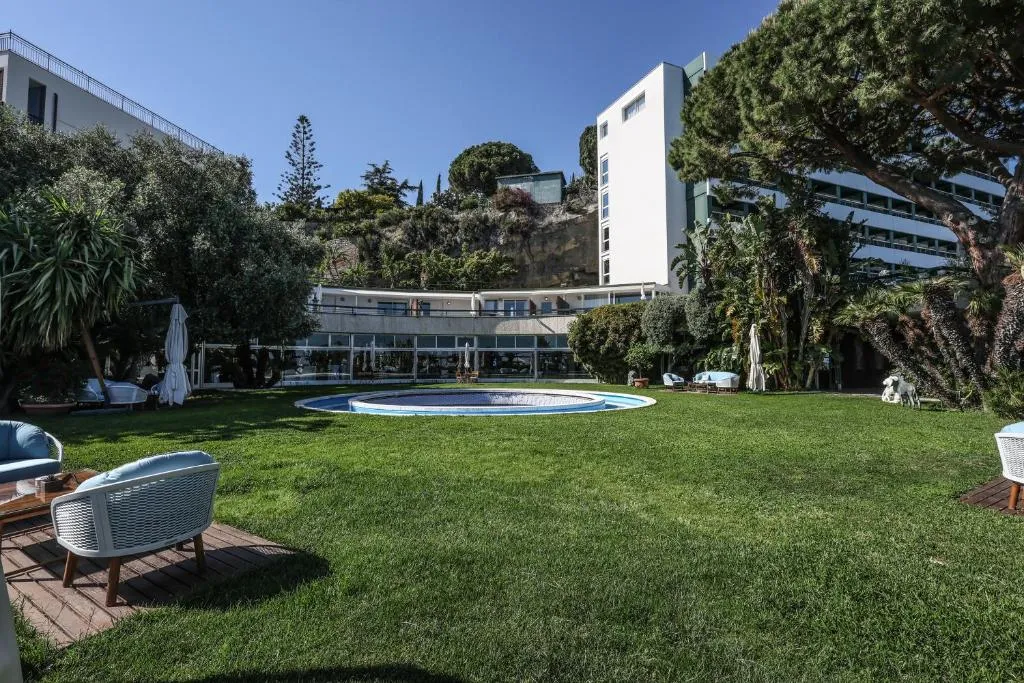 Ampio giardino verde con piccola piscina circolare e hotel sullo sfondo