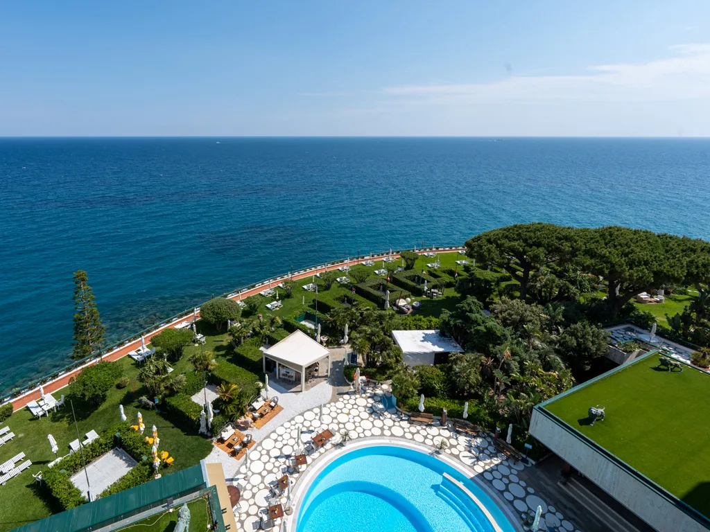 Vista panoramica dall'alto della piscina e del giardino con il mare blu all'orizzonte