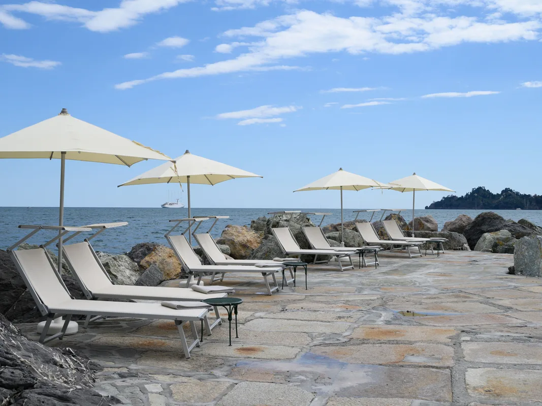Solarium sugli scogli con lettini e ombrelloni bianchi affacciati sul mare