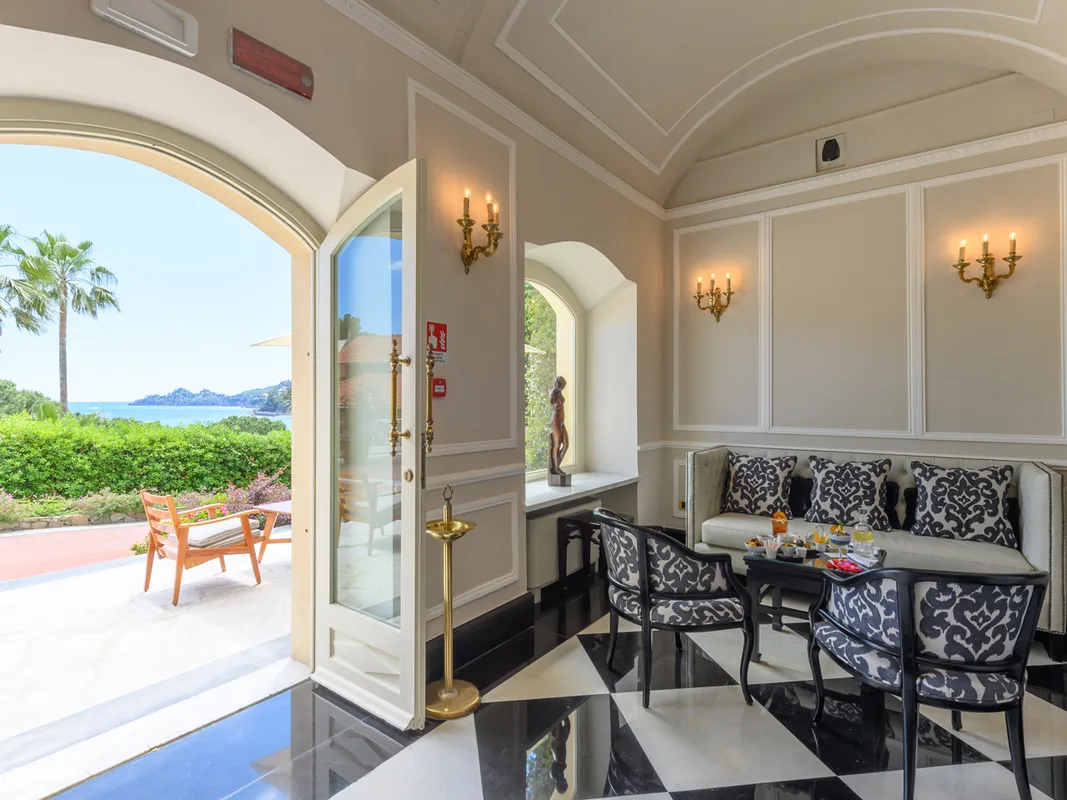 Salottino interno con pavimento a scacchi, divano elegante e porta aperta sulla terrazza con vista mare