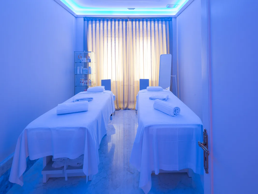 Cabina spa con due lettini per massaggi, asciugamani arrotolati e illuminazione blu rilassante