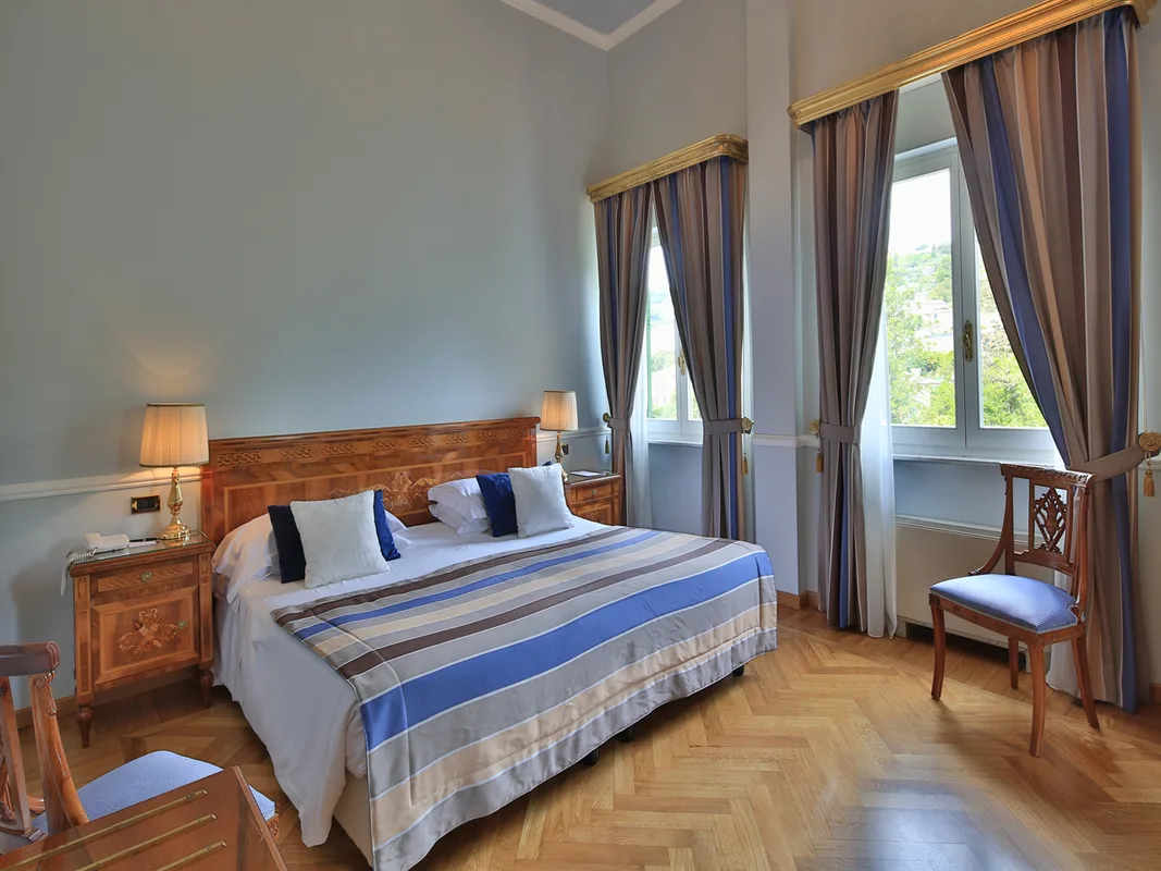Camera elegante con letto matrimoniale, testiera in legno intarsiato e finestre con vista