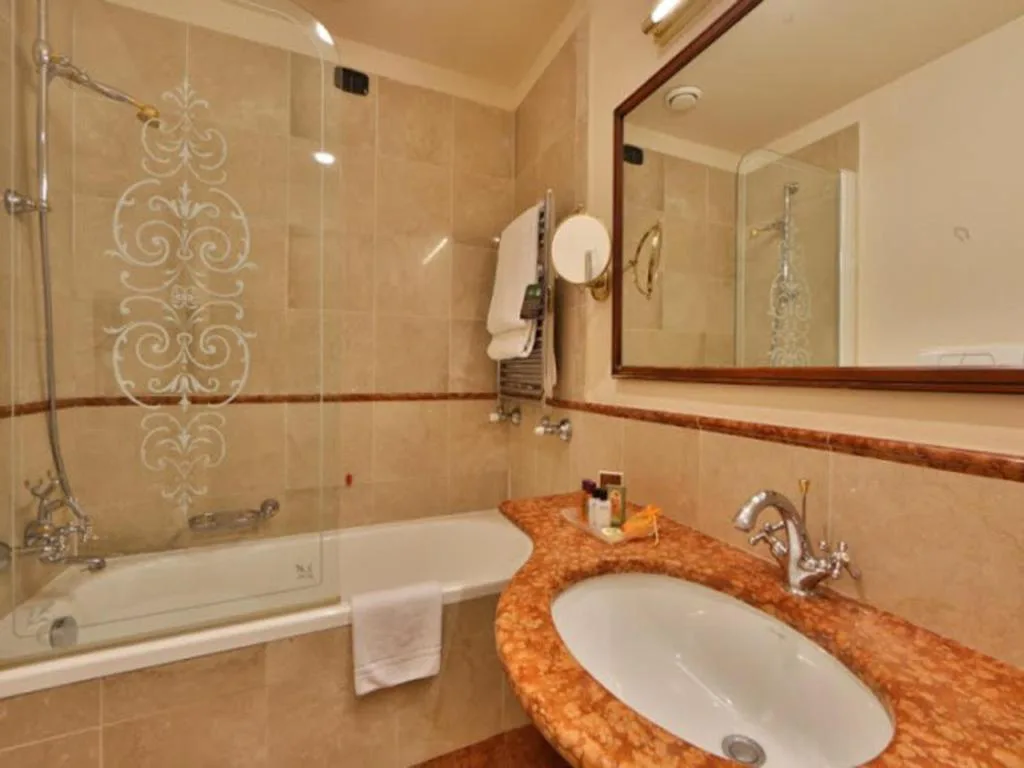 Bagno elegante con vasca dal vetro decorato e lavabo in marmo arancione