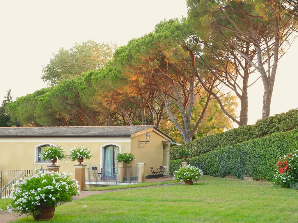 Edificio giallo immerso nel verde con pini, giardino fiorito e vialetto
