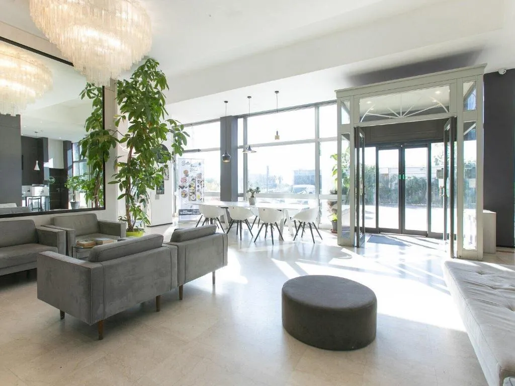 Hall luminosa con poltrone grigie, grande pianta verde e lampadari di cristallo