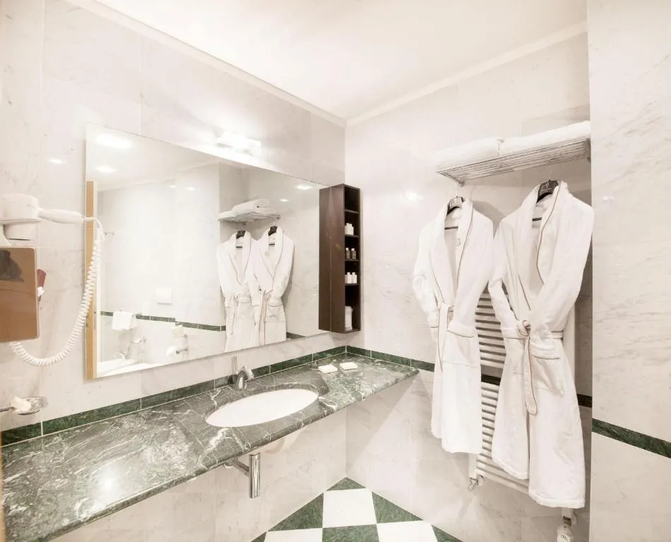 Bagno elegante in marmo verde e bianco con grande specchio, lavabo e accappatoi bianchi