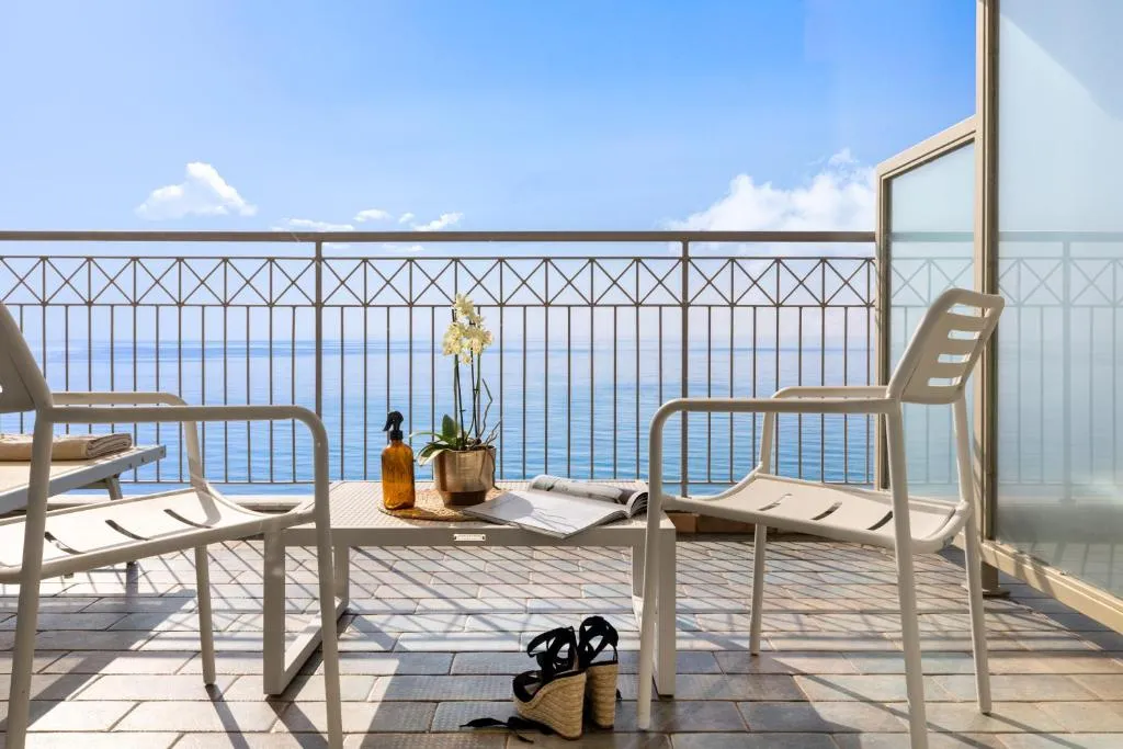 Balcone con sedie bianche e tavolino affacciato sul mare azzurro