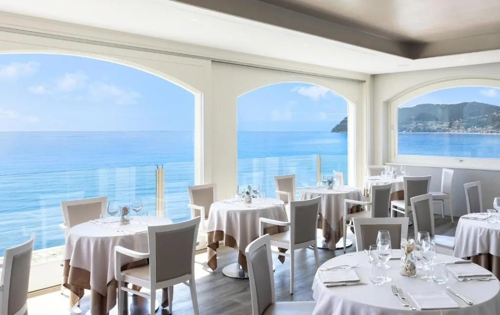 Sala ristorante luminosa con tavoli bianchi e ampie finestre ad arco affacciate sul mare