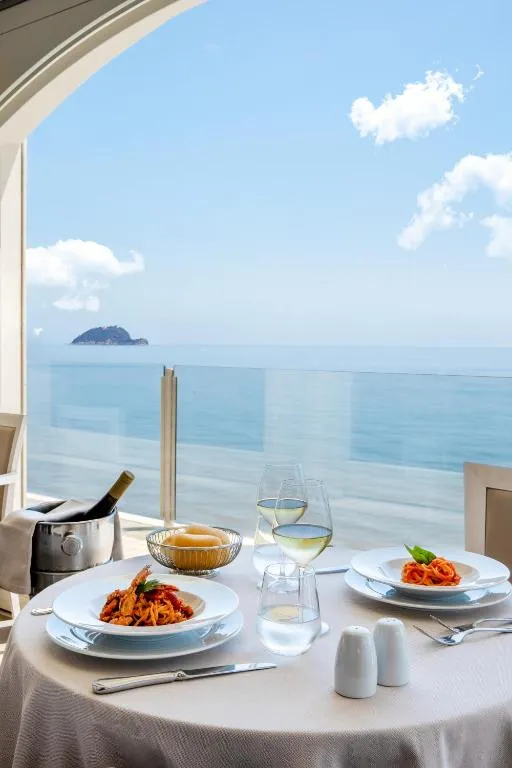 Tavolo del ristorante con piatti di pasta e vino bianco affacciato sul mare e isola