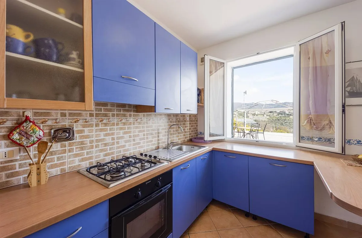 Cucina angolare con mobili blu, piano cottura a gas e finestra panoramica sulle colline