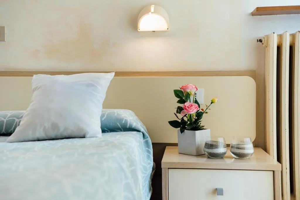 Dettaglio comodino con fiori rosa e applique sopra il letto