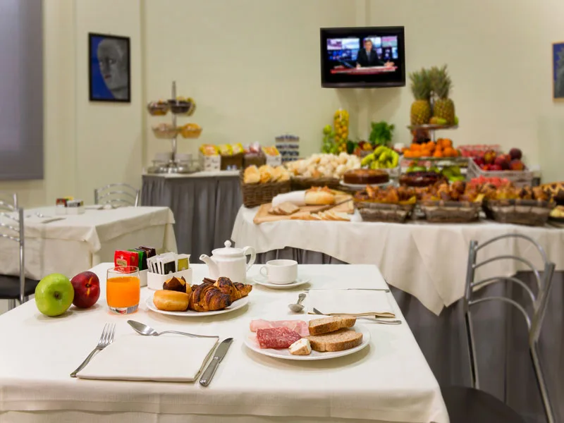 Tavolo apparecchiato per la colazione con buffet di dolci e frutta sullo sfondo