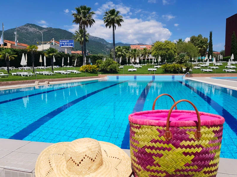 Bordo piscina con cappello di paglia e borsa colorata, lettini e palme