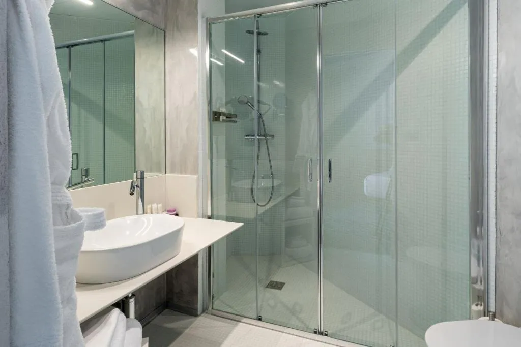 Bagno con ampia doccia in vetro, lavabo da appoggio bianco e grande specchio a parete