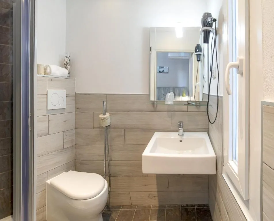 Bagno con lavabo bianco, specchio, asciugacapelli e piastrelle effetto legno