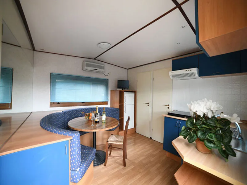 Zona pranzo di mobile home con panca curva blu, tavolo e cucina attrezzata