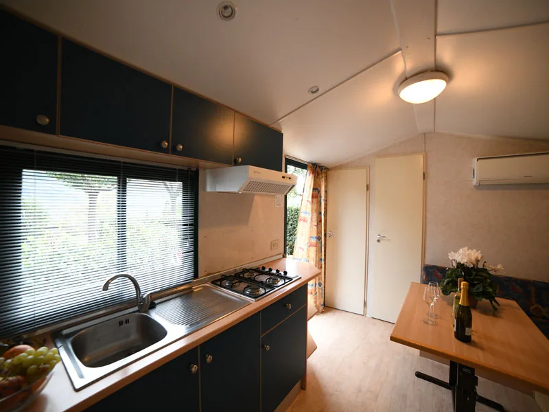 Cucina di mobile home con piano cottura, lavello e zona pranzo accanto alla finestra