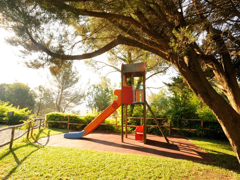 Area giochi per bambini con scivolo immersa nel verde e alberi al tramonto
