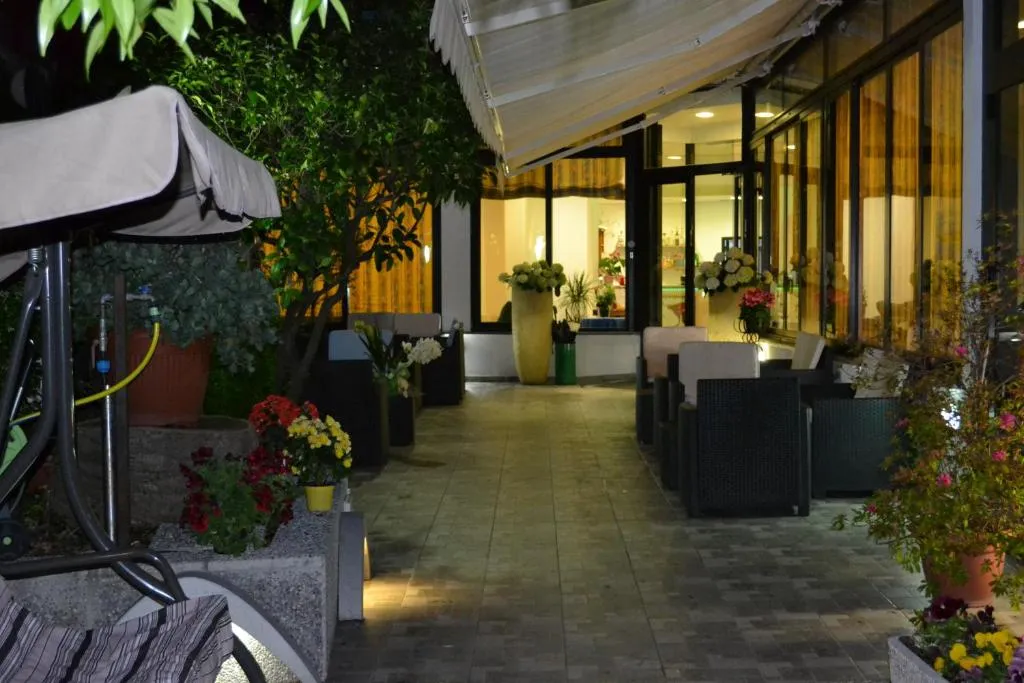 Cortile esterno illuminato in serata con poltrone in rattan, piante fiorite e ingresso dell'hotel sullo sfondo