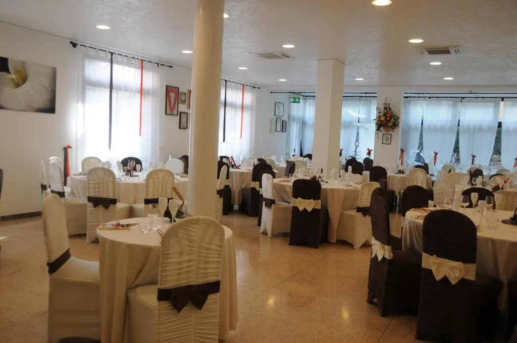 Sala ristorante allestita per banchetto con tavoli rotondi e sedie rivestite con fiocchi bianchi e marroni